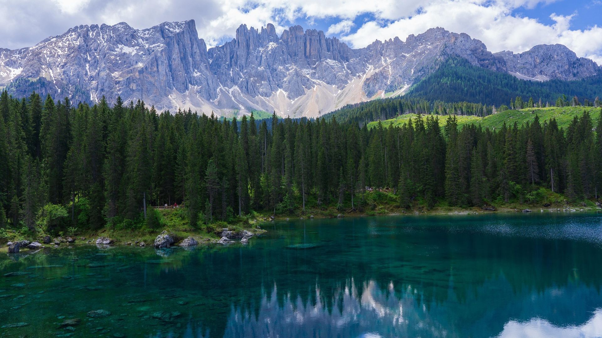Clear freshwater lake surrounded by dense coniferous forest with rocky mountains reflected on the calm water surface.